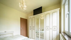 Un dormitorio con cama, armario, espejo, candelabro y radiador.