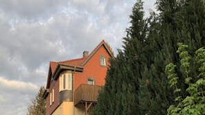 Una casa de dos pisos con un balcón de madera, rodeada de un bosque frondoso.