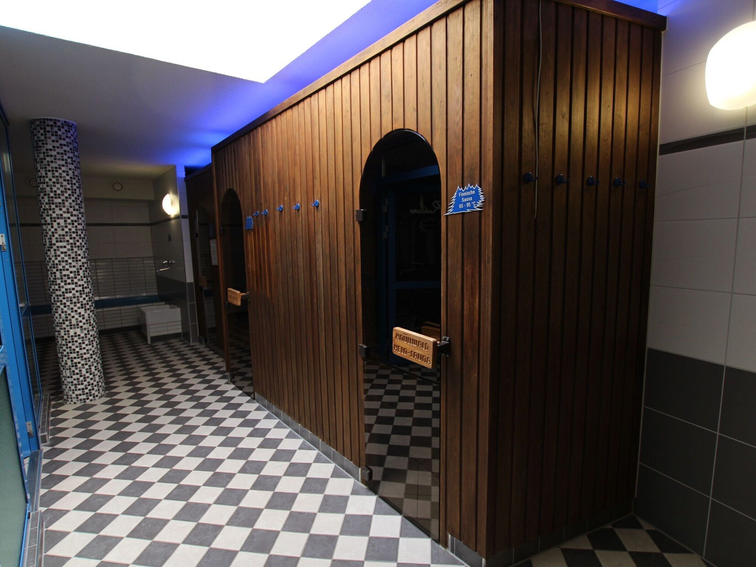A public restroom with a checkered floor, wooden partitions, and a sign indicating a temperature of 65-95°C.