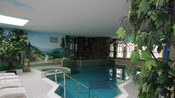 Una piscina interior con suelo de baldosas, piscina de color azul y un mural en la pared con una escena de bosque.