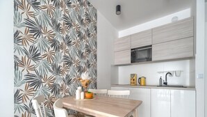 A modern kitchen with white cabinets, a wooden dining table, and a patterned wallpaper. - Apartment in Rewal Near Baltic Sea Beach (Rewal)