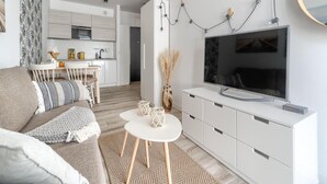 A modern living room with a sofa, coffee table, and TV. There's a kitchen in the background with white cabinets and a dining area. - Apartment in Rewal Near Baltic Sea Beach (Rewal)