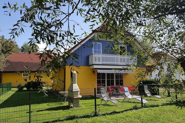 A two-story building with a balcony, a fenced yard, and outdoor seating. - Ferienhauser am Kummerower See, Verchen (Verchen)