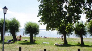 A grassy area with trees and a lamp post, near a body of water. - Ferienhauser am Kummerower See, Verchen (Verchen)