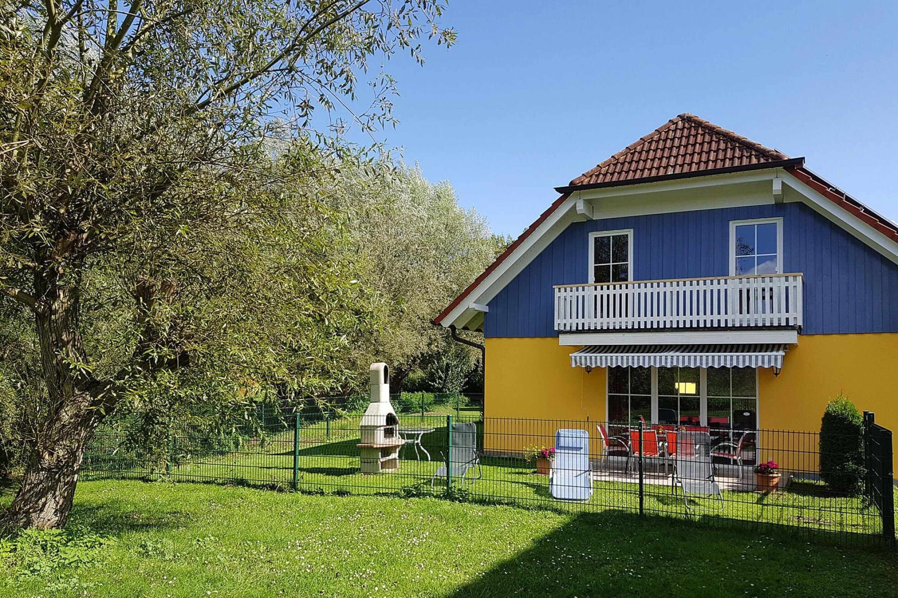 A two-story house with a blue and yellow exterior, a balcony, and a fenced backyard with outdoor furniture.