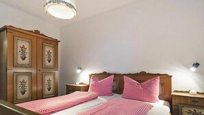 Egy franciaágy, kockás mintájú ágytakaróval és hozzáillő párnákkal, fafejtámlával, éjjézőasztalokkal, melyeken lámpák állnak, és egy díszes, virágmintás szekrény.