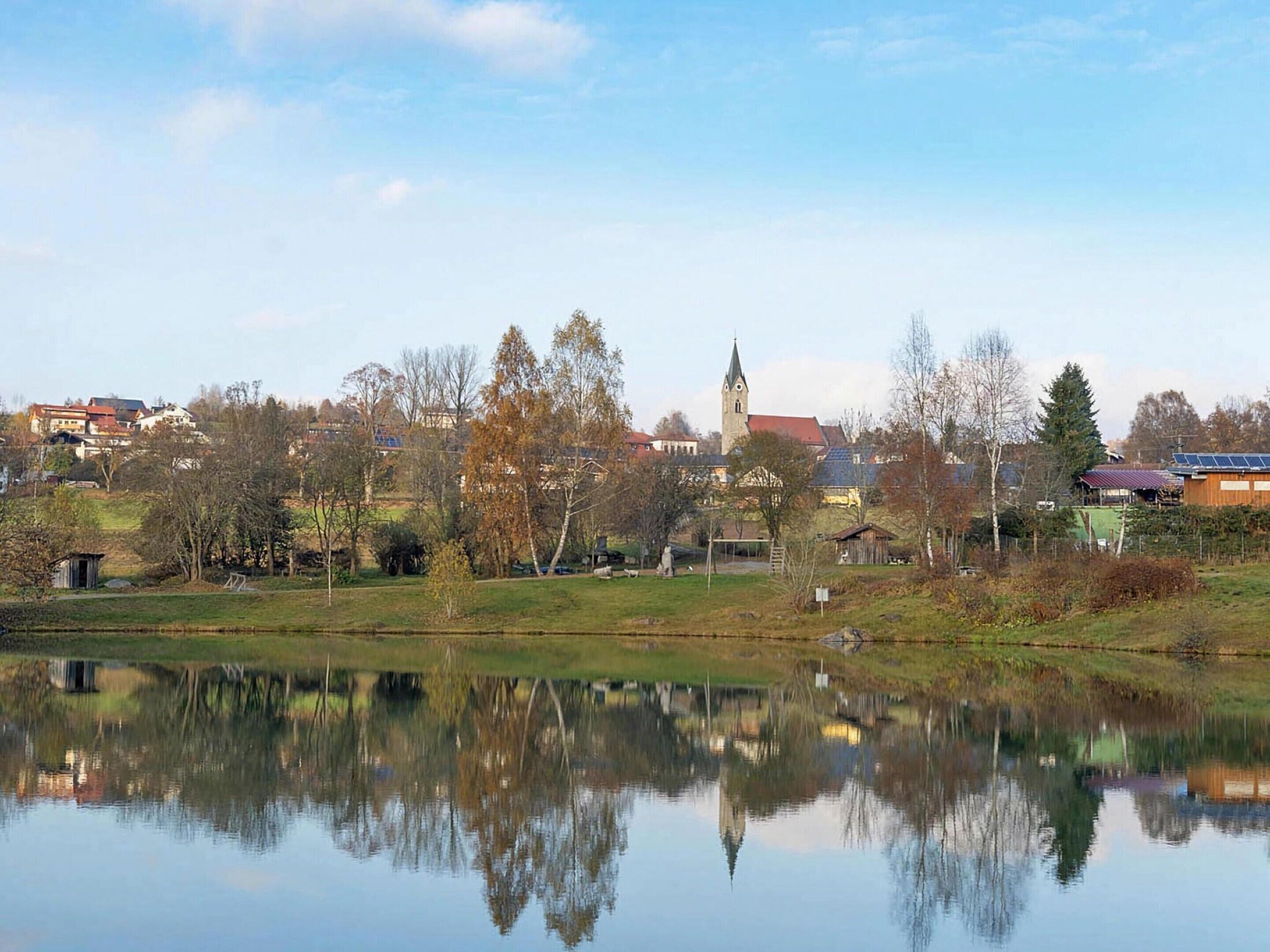 Tyyni järvi, jonka pinnasta heijastuvat rakennukset ja puut, ja kauempana näkyy kirkontorni.