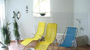 A room with two yellow-striped lounge chairs, a blue chair, a potted plant, a life preserver, and a window with a sailboat. - Chalet in Radstadt Near Ski Slopes & Spa (Radstadt)