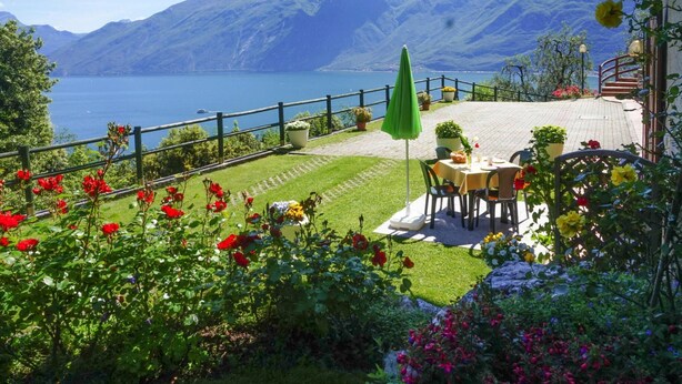 Eine Terrasse mit Tisch und Stühlen mit Blick auf einen See und Berge.