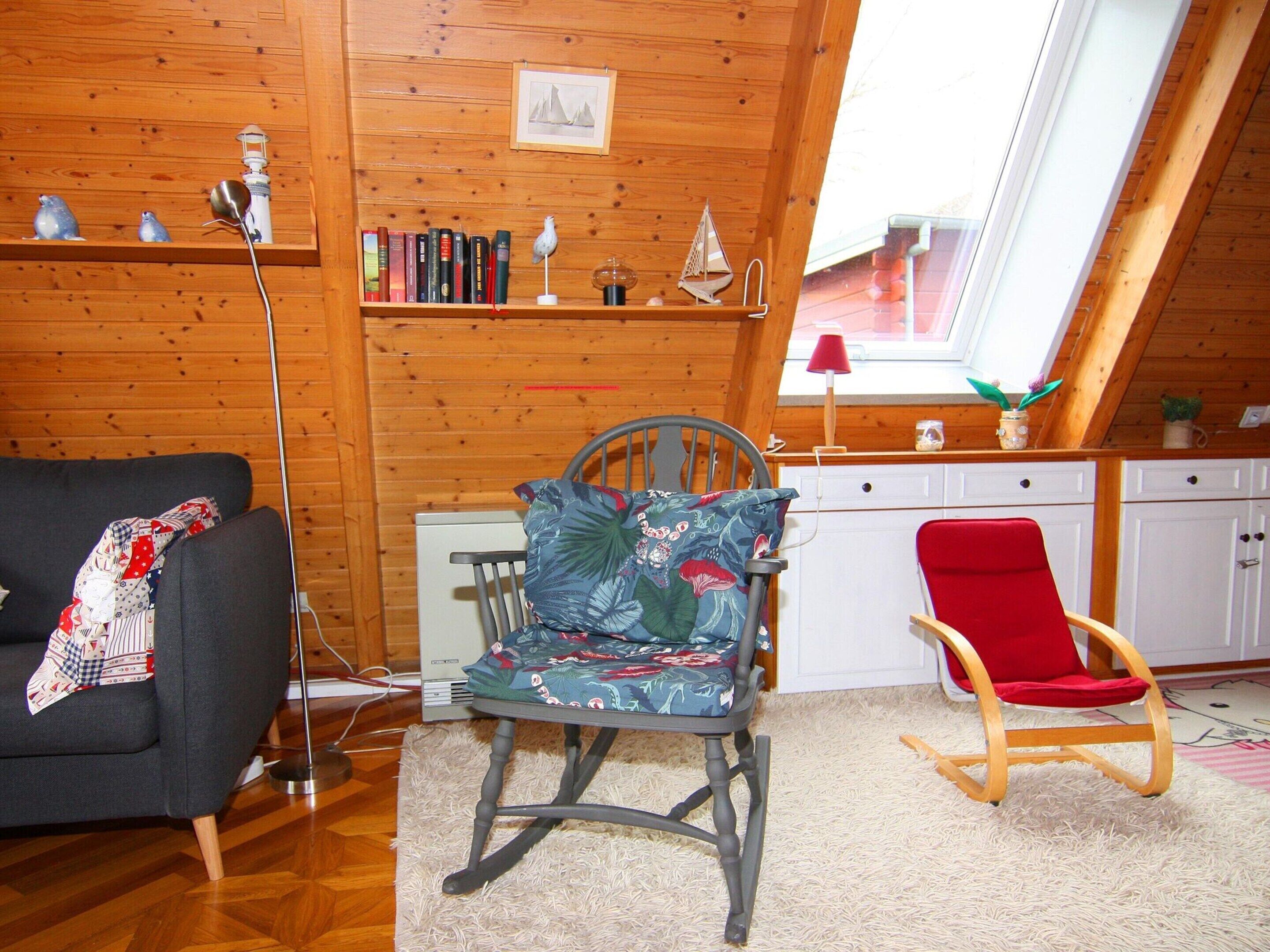 A cozy room with a wooden ceiling, a bookshelf, a desk, a red chair, and a rocking chair.