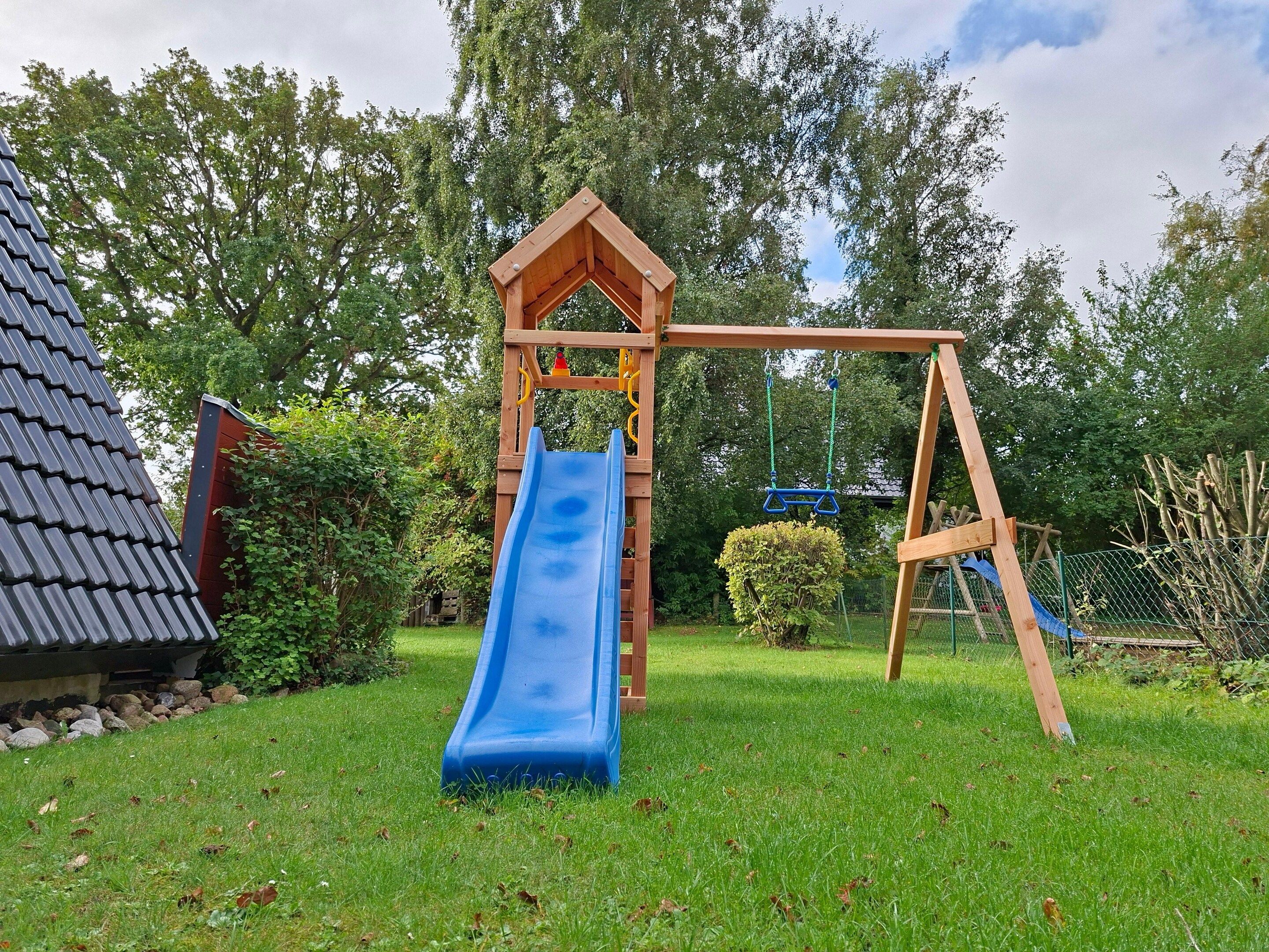 Eine hölzerne Spielanlage mit einer blauen Rutsche und Schaukeln in einem grünen Rasen.