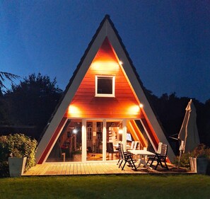 A triangular wooden house with a small window and a porch with chairs and a table. - Gemutliches Ferienhaus an der Ostsee in Damp (Damp)