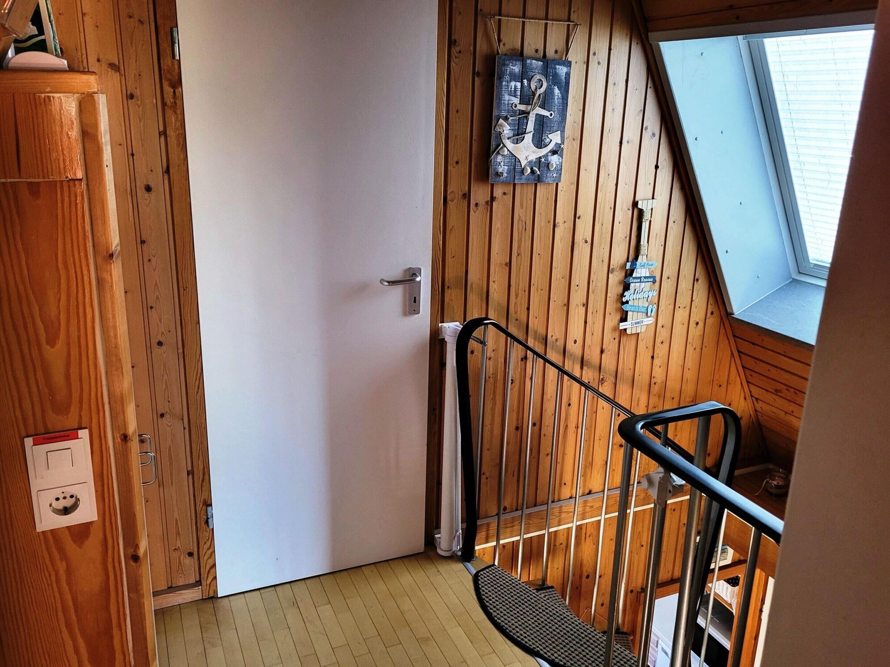 A wooden interior with a door, a metal handrail, and a window.