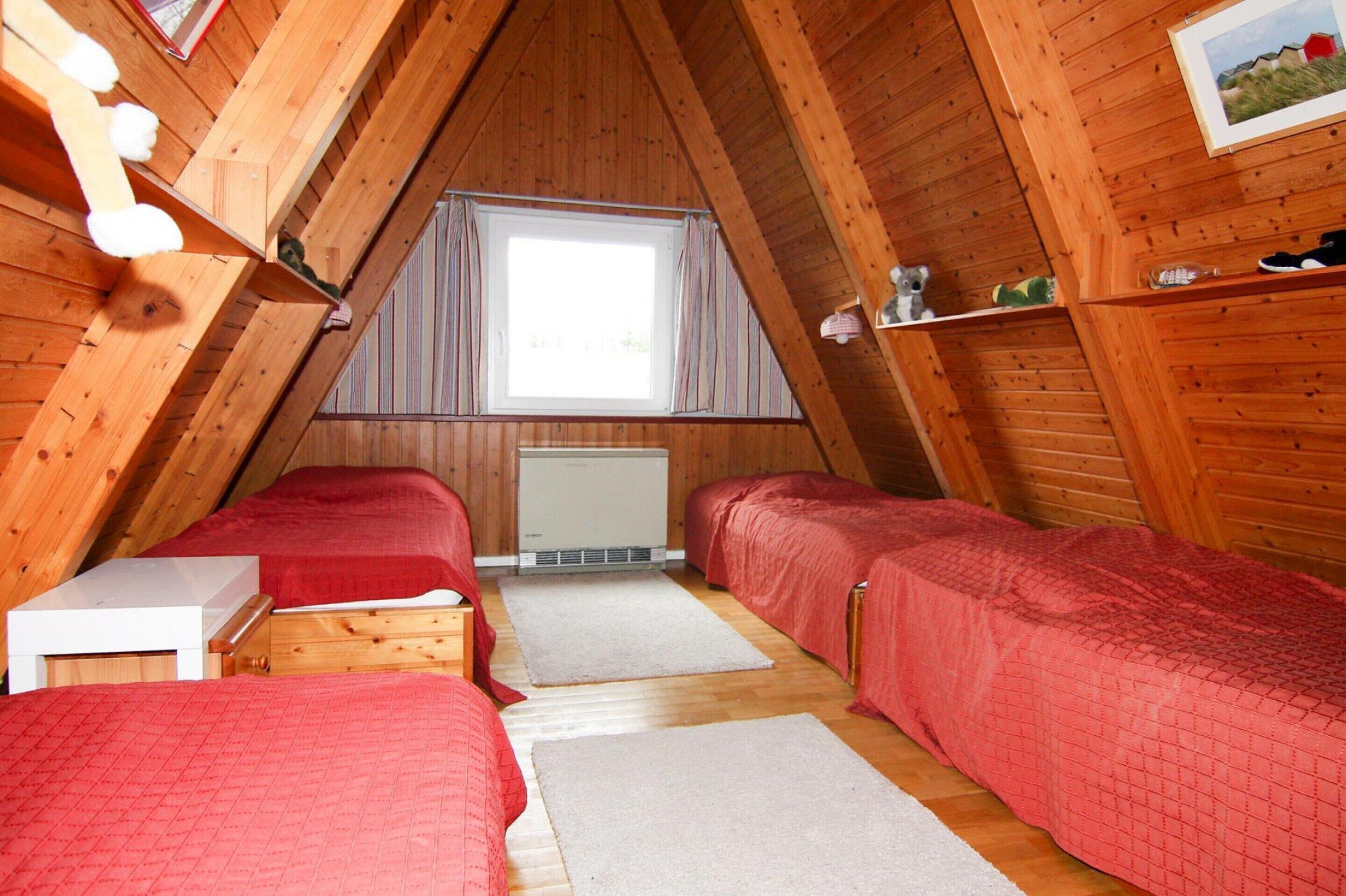 A small, wooden attic bedroom with two beds, a window with curtains, and a radiator.
