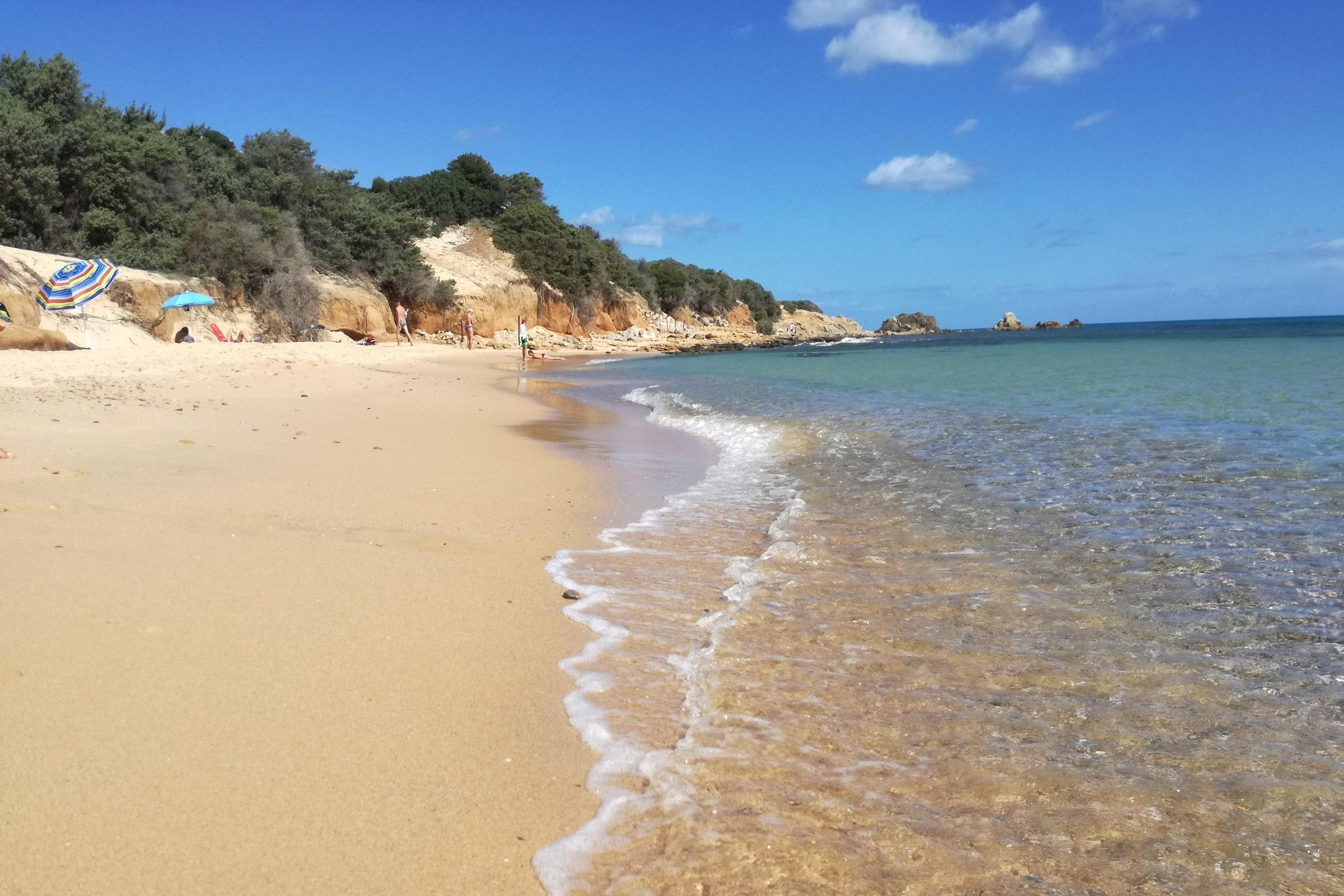 A beach with clear water, sandy shore, and rocky cliffs.