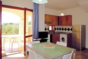 A compact kitchen with wooden cabinets, a built-in washing machine, and a refrigerator. - Apartment in Villaputzu With Garden (Domus de Maria)