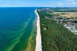 An aerial view of a coastal area with a beach, dense forest, and residential buildings. - Holiday Apartment Near the Sea, Pustkowo (Rewal)