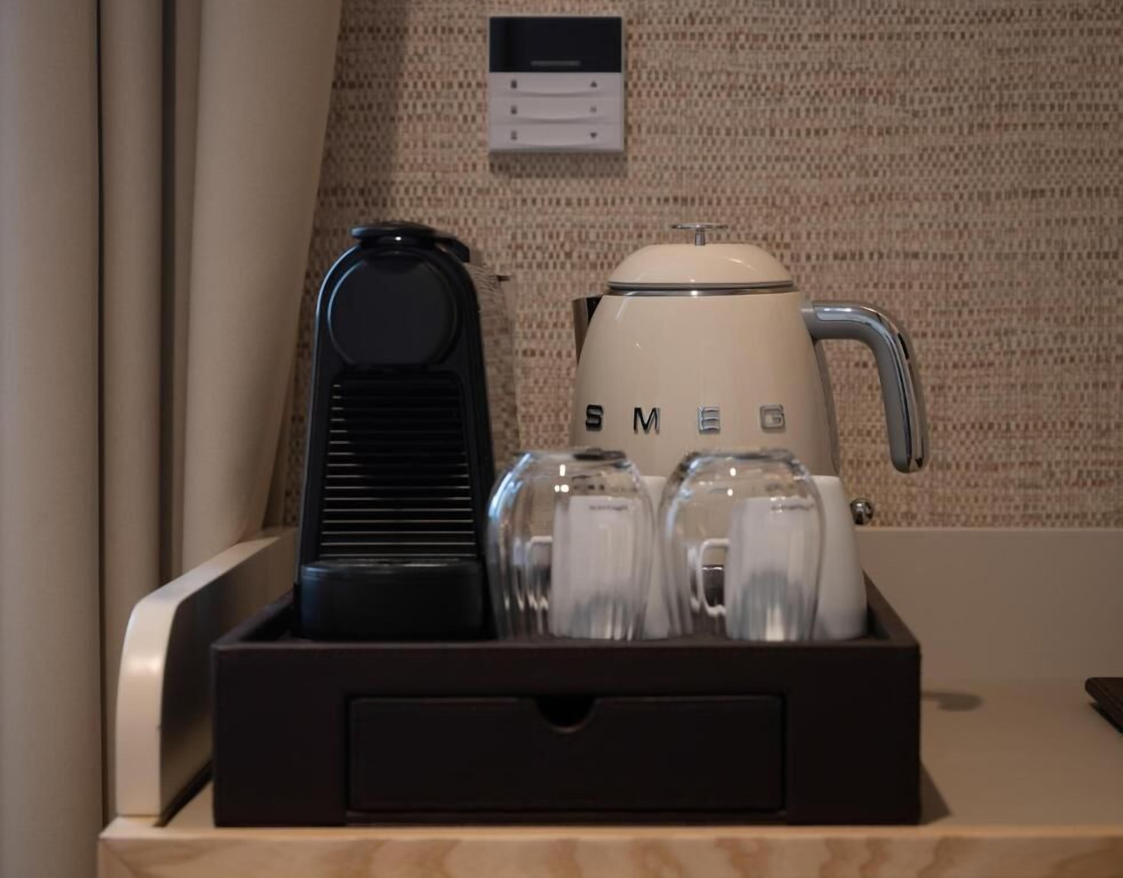 A coffee maker, a kettle, and four glasses in a tray on a counter.