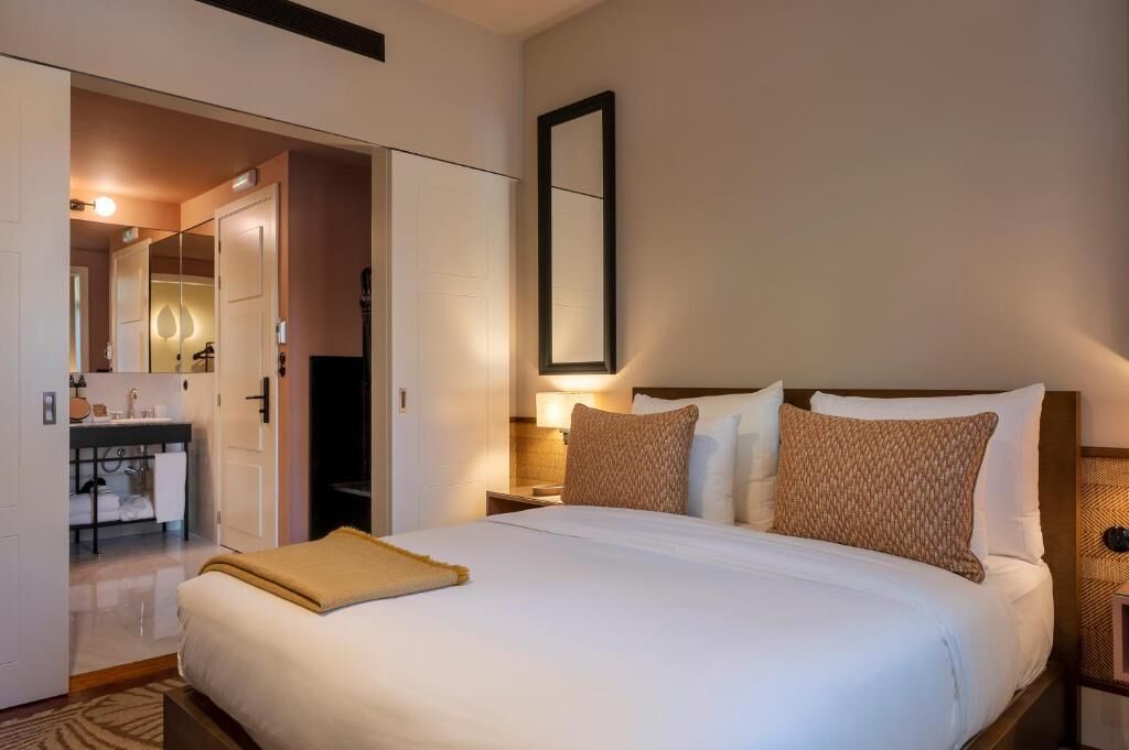 Camera d'albergo con un letto grande, un comodino, uno specchio e un bagno visibile attraverso una porta aperta.