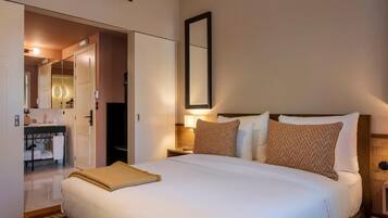 Camera d'albergo con un letto grande, un comodino, uno specchio e un bagno visibile attraverso una porta aperta.