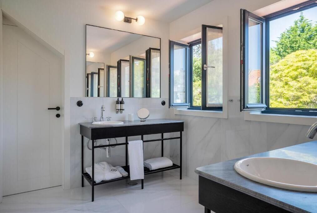 A modern bathroom with a large mirror, a black vanity, and a window providing a view of greenery outside.
