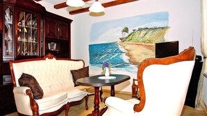 A living room with a white sofa, a wooden armchair, a small round table with a vase, and a painting of a beach scene on the wall. - Ferienwohnung, Ribnitz-damgarten (Ribnitz-Damgarten)