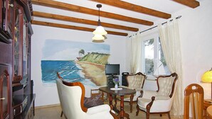 A dining area with a table and four chairs, a painting of a beach scene on the wall, and a wooden ceiling with exposed beams. - Ferienwohnung, Ribnitz-damgarten (Ribnitz-Damgarten)