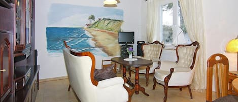 A dining area with a table and four chairs, a painting of a beach scene on the wall, and a wooden ceiling with exposed beams.