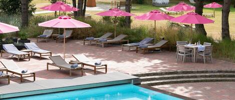 A poolside area with lounge chairs and umbrellas, a pool, and a grassy area with trees.