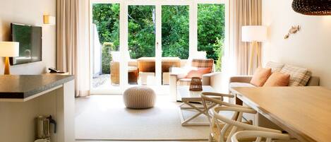 Une chambre d’hôtel moderne dotée d’un coin repas, d’une télévision et offrant une vue sur la verdure.