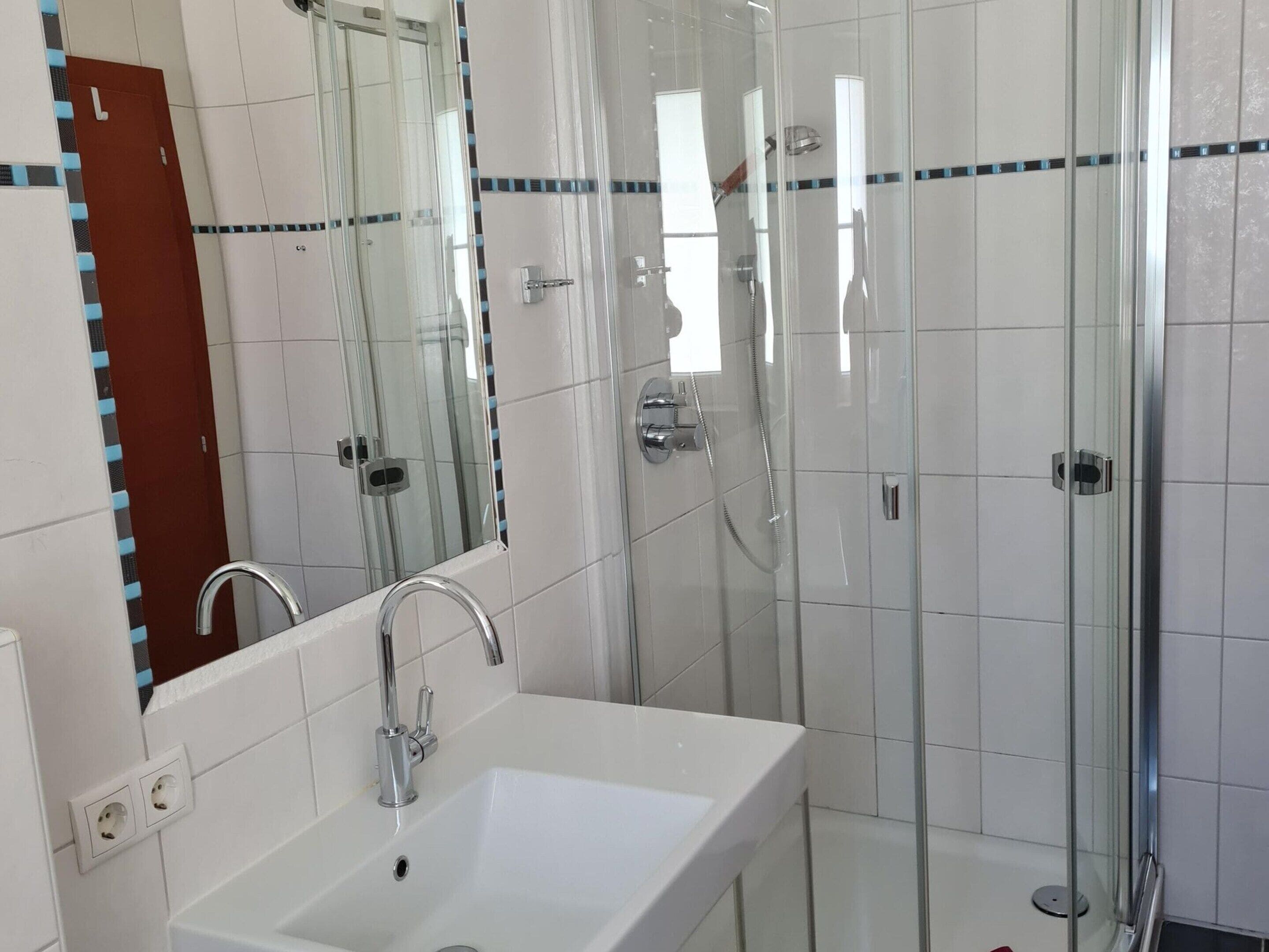A bathroom with a white sink, a mirror, and a glass-enclosed shower area.