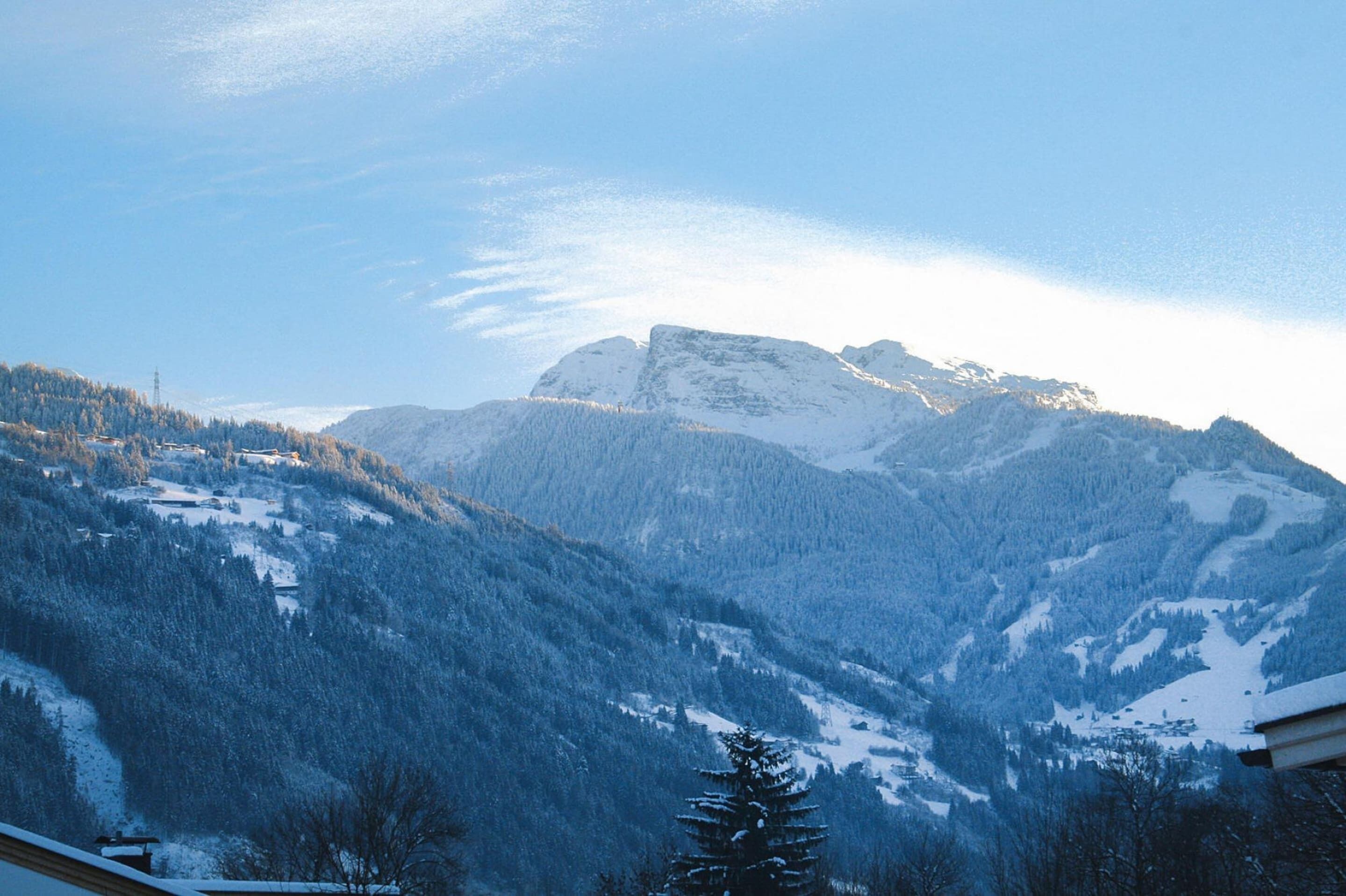Un paisaje montañoso con picos nevados y un valle boscoso.