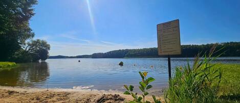 A lakeside view with a signboard, calm water, and a clear sky.