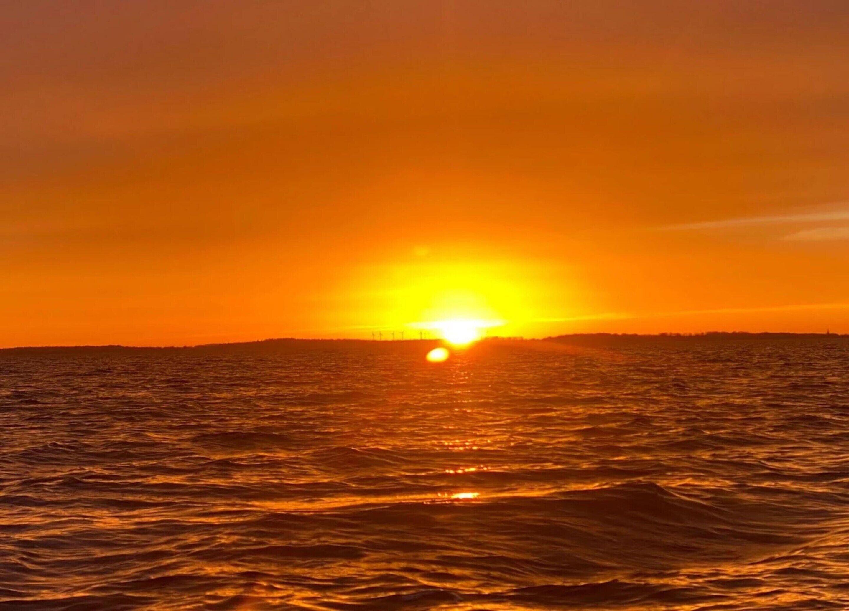 Ein Sonnenuntergang über einem Gewässer mit einer fernen Küstenlinie.