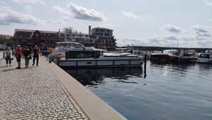 A marina with boats docked, a cobblestone walkway, and buildings in the background. - Studio in Buchholz am Mueritzsee (Buchholz)