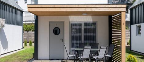 A modern house with a covered patio, a dining table with chairs, and a small garden area.