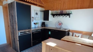 A compact kitchen with modern appliances, a wooden dining table, and a small seating area. - Rossweid hut With a Fantastic View (Stans)