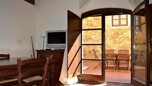 A room with a wooden dining table and chairs, a television, and a view of an outdoor patio with stone walls and a wooden table and chairs. - Campiglia Apartment Near Nature (Campiglia Marittima)