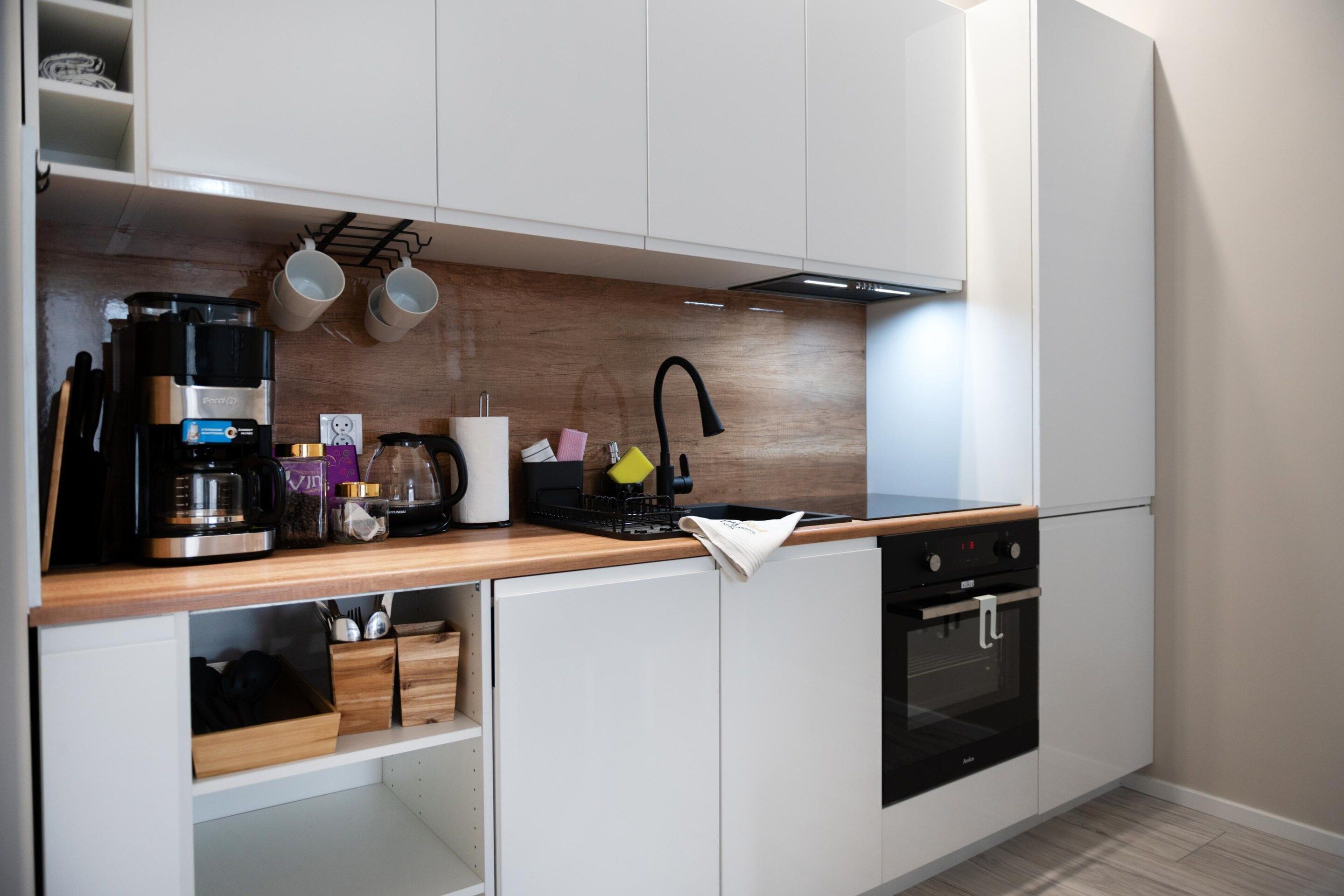 A modern kitchen with white cabinetry, a wooden countertop, a coffee maker, a kettle, and a built-in oven.