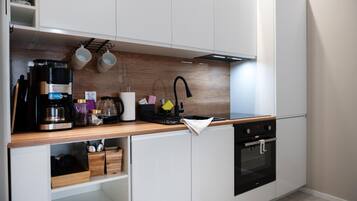 A modern kitchen with white cabinetry, a wooden countertop, a coffee maker, a kettle, and a built-in oven.