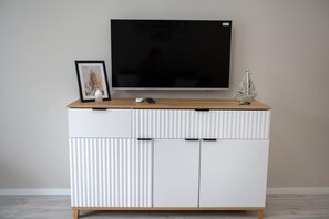 A modern entertainment unit with a flat-screen TV, a framed picture, a small vase, and a decorative ship model. - Apartment With air Conditioning, Pool, Sauna (Dziwnów)