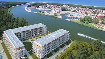 Un hôtel moderne doté d’une terrasse sur le toit, situé au bord d’une rivière, avec un port de plaisance et un quartier résidentiel en arrière-plan.