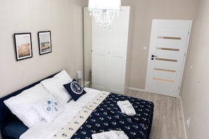 A bedroom with a bed, two framed pictures, a chandelier, and a white door. - Apartment With air Conditioning, Pool, Sauna (Dziwnów)