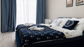 A neatly made bed with a navy blue and white anchor pattern bedspread, white pillows, and a matching throw blanket. - Apartment With air Conditioning, Pool, Sauna (Dziwnów)