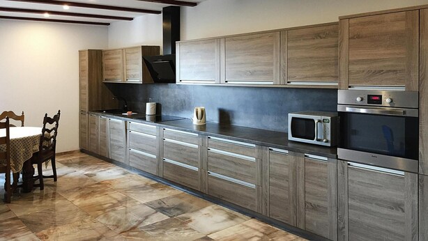A modern kitchen with wooden cabinets, a microwave, and a built-in oven. - Comfortable XXL Holiday Villa by the Pond (Malechowo)