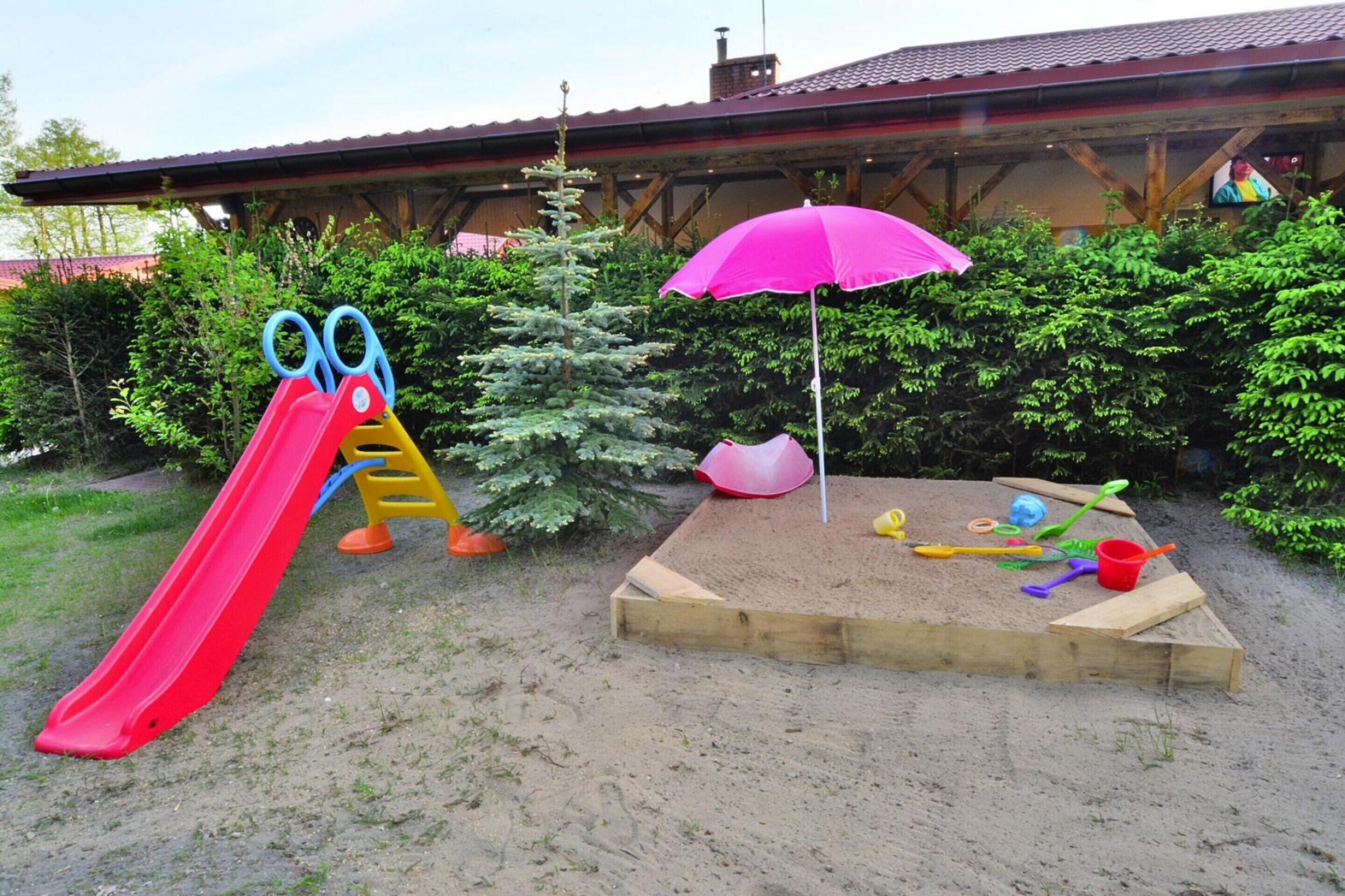 A playground with a red slide and a sandpit with toys.