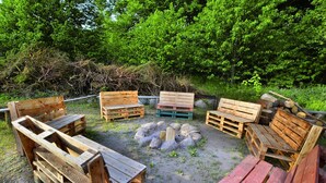 A rustic outdoor seating area with wooden benches and a central fire pit surrounded by rocks. - Comfortable XXL Holiday Villa by the Pond (Malechowo)