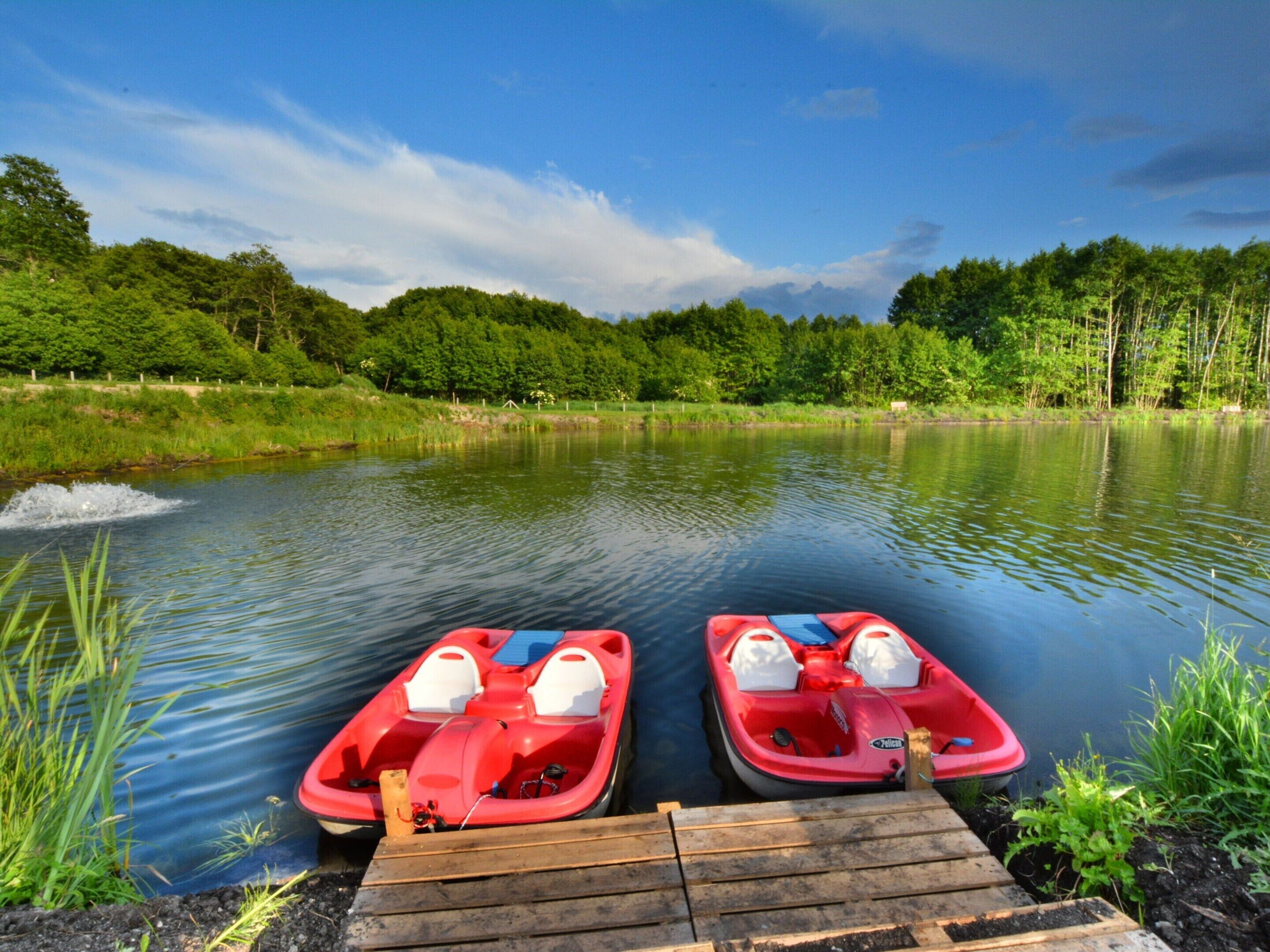 Two red boats docked at a wooden pier with a calm lake and forested hills in the background.