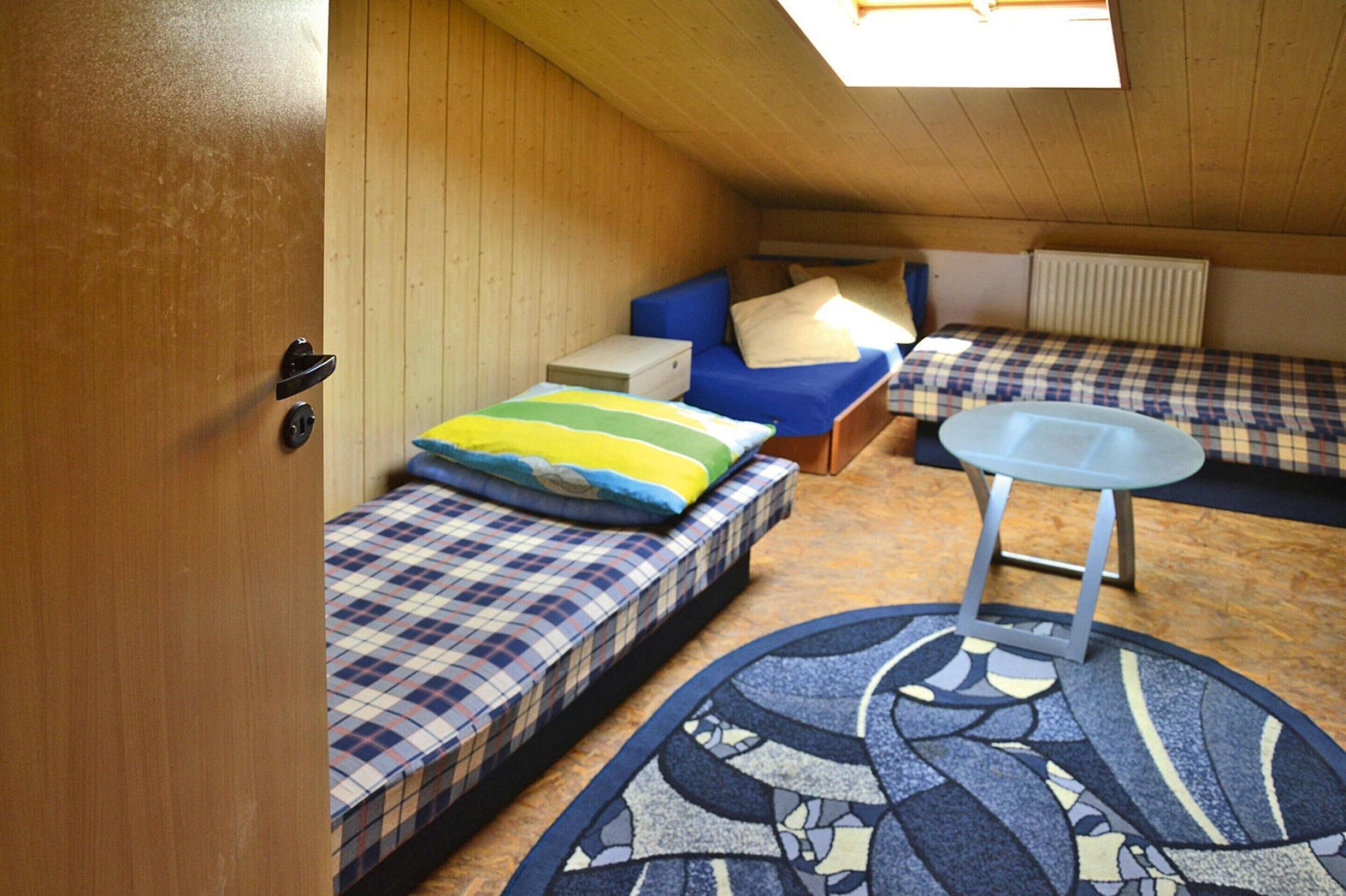 Ett litet rum med två sängar, ett litet bord och ett takfönster.