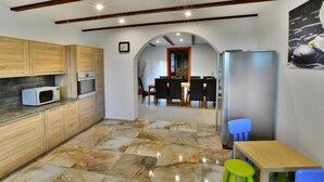 A kitchen with wooden cabinets, a microwave, and a refrigerator. There is a dining area with a table and chairs, and a small stool. - Comfortable XXL Holiday Villa by the Pond (Malechowo)